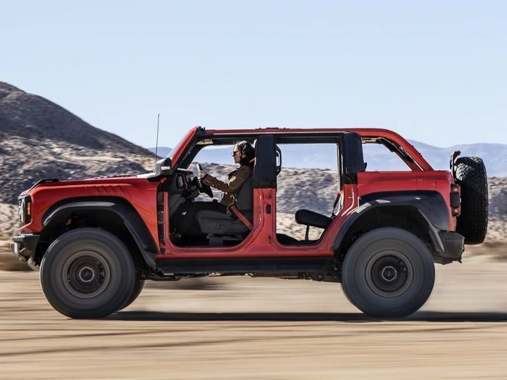 Four door 2022 Ford Bronco Raptor shown in Hot Pepper Red being driven in a desert with top and doors removed 