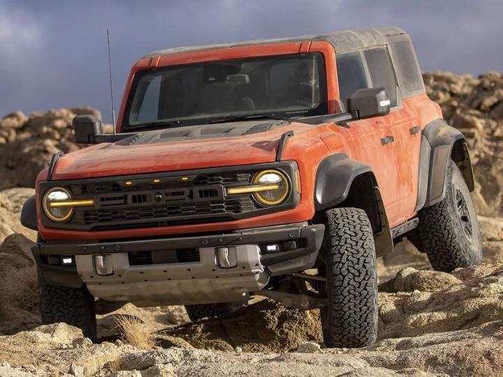 Four door 2022 Ford Bronco Raptor shown in Hot Pepper Red being driven in a desert with top and doors removed