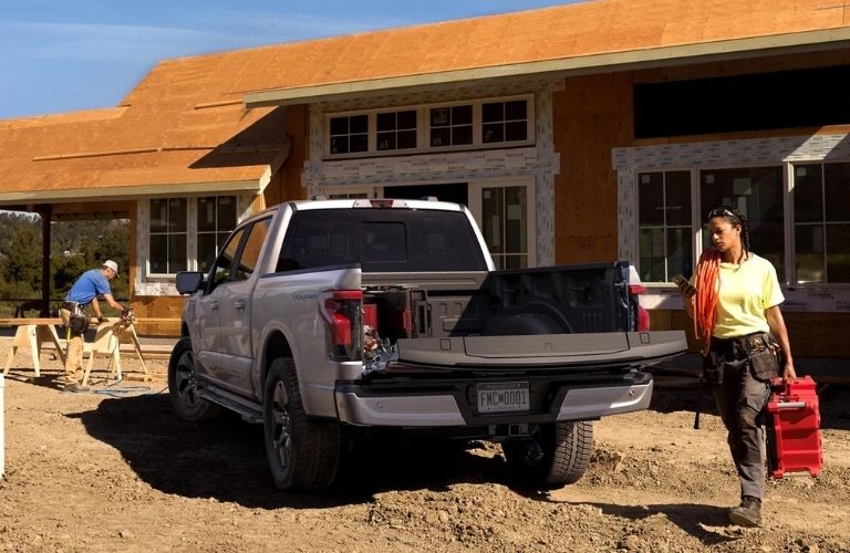 Rear view of a Ford F-150 Lightning with open tailgate as a woman carrying cargo walks past