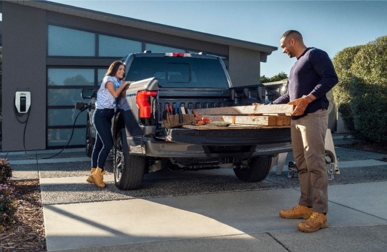 Image showing a man loading wooden logs on the truck bed of the Ford F-150 Lightning as a woman watches
